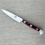 A Gude Micarta paring knife with steel blade and a marbled red, black handle displayed diagonally on a light gray wood-grain surface.